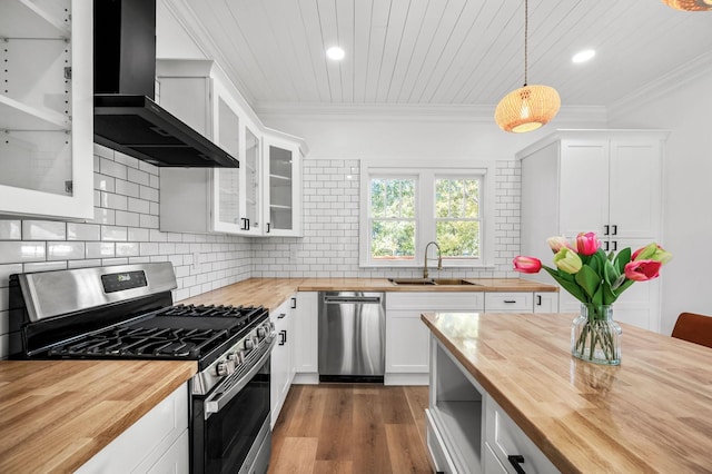 kitchen featuring wall chimney exhaust hood, sink, white cabinetry, pendant lighting, and stainless steel appliances