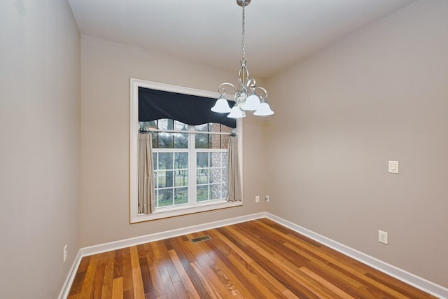 spare room with hardwood / wood-style flooring and an inviting chandelier