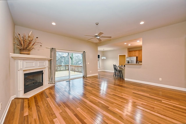 unfurnished living room with a premium fireplace, ceiling fan, and light wood-type flooring