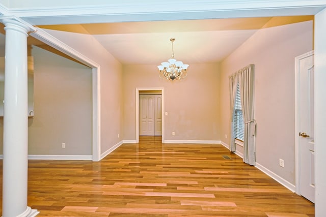 empty room featuring an inviting chandelier, light hardwood / wood-style flooring, and decorative columns