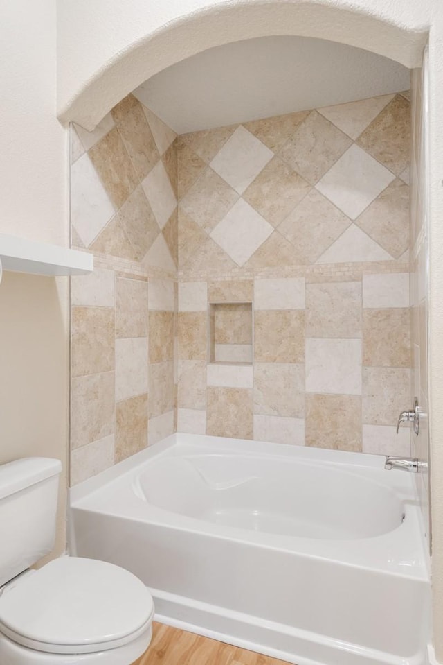 bathroom with hardwood / wood-style flooring, tiled shower / bath, and toilet