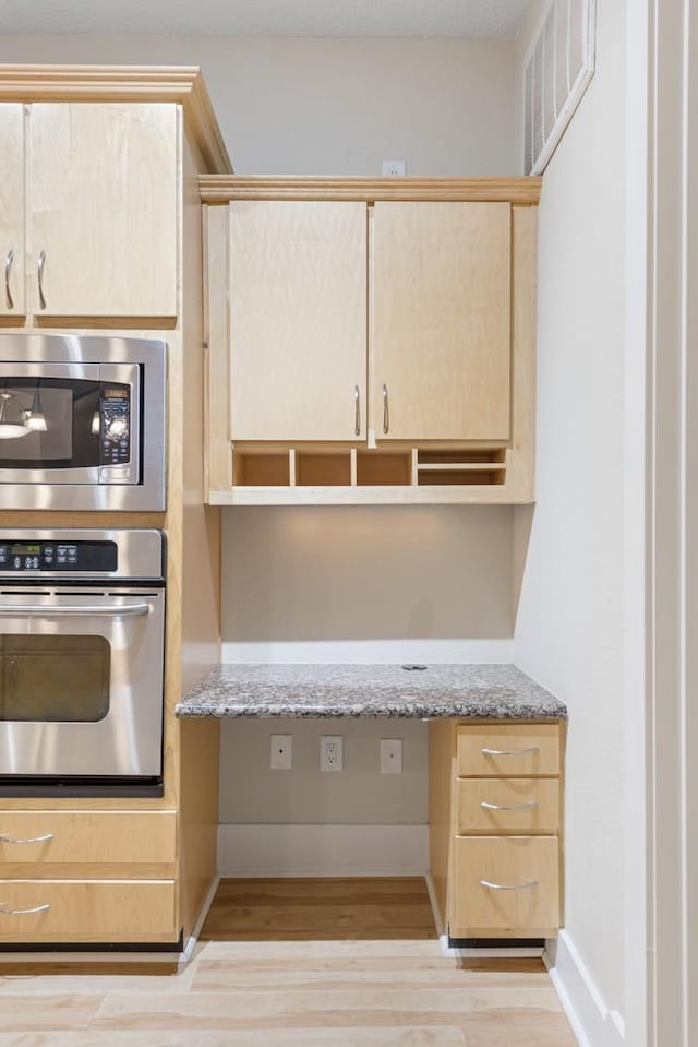 kitchen with light stone countertops, appliances with stainless steel finishes, built in desk, and light brown cabinets