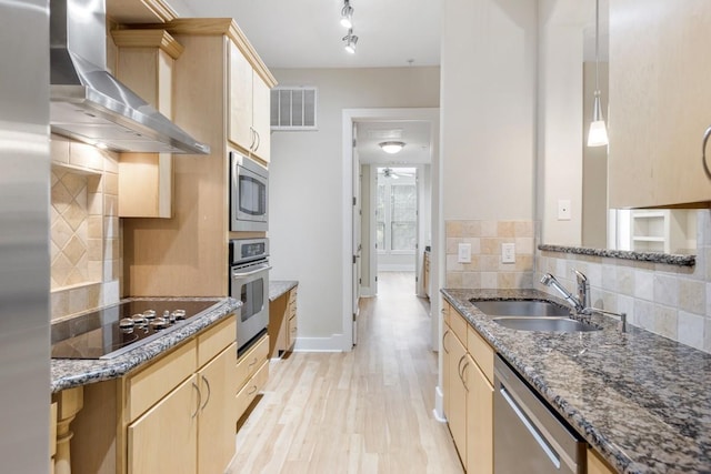 kitchen with light brown cabinetry, sink, dark stone countertops, stainless steel appliances, and wall chimney range hood