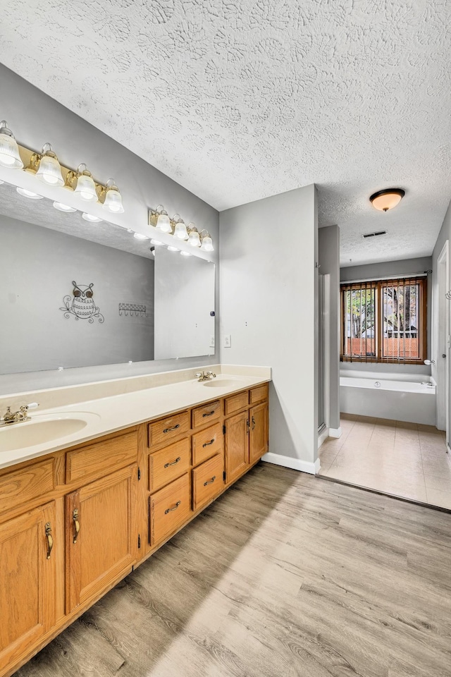 bathroom with vanity, a bath, hardwood / wood-style flooring, and a textured ceiling