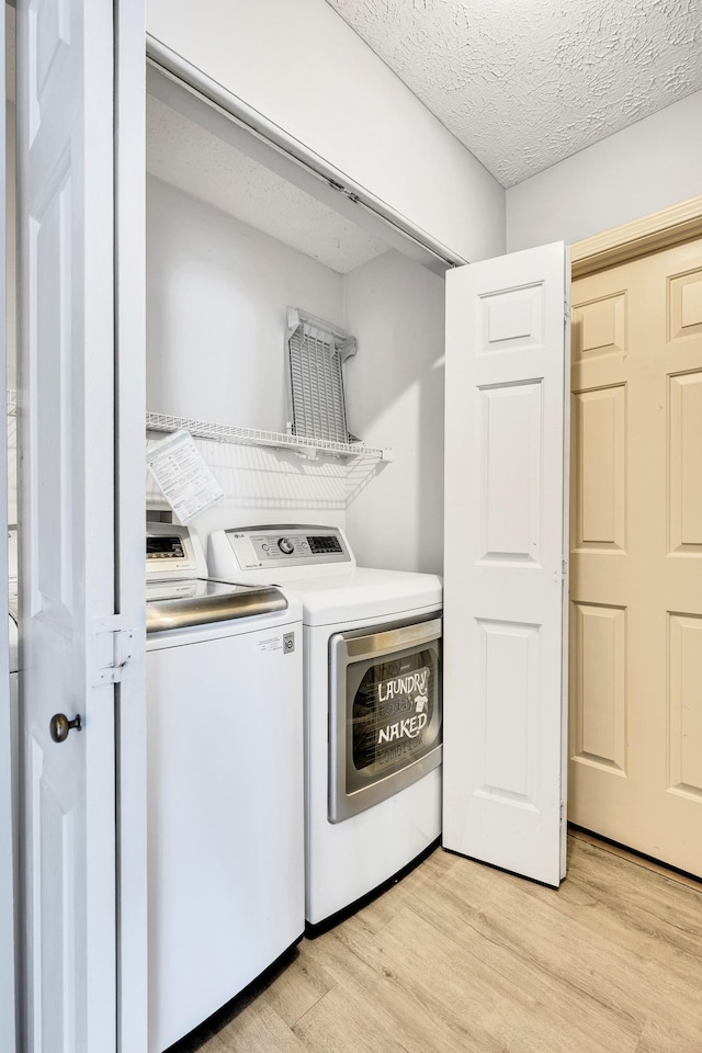 laundry room featuring independent washer and dryer, light hardwood / wood-style floors, and a textured ceiling