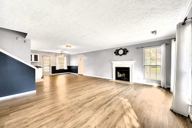 unfurnished living room featuring ceiling fan, ornamental molding, a textured ceiling, and light hardwood / wood-style floors