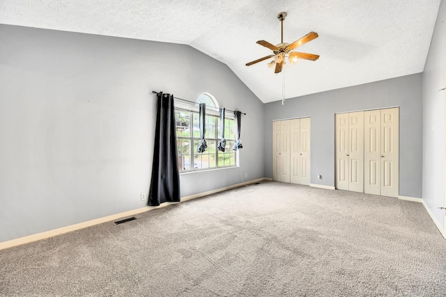 unfurnished bedroom featuring multiple closets, lofted ceiling, carpet flooring, and a textured ceiling