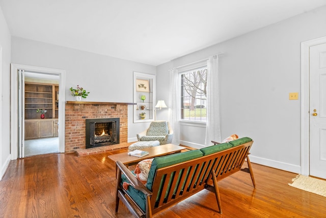 living room with a brick fireplace, hardwood / wood-style floors, and built in shelves