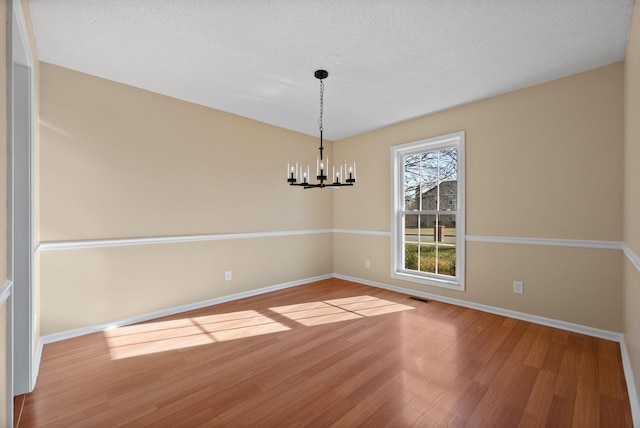 empty room with an inviting chandelier, wood-type flooring, and a textured ceiling