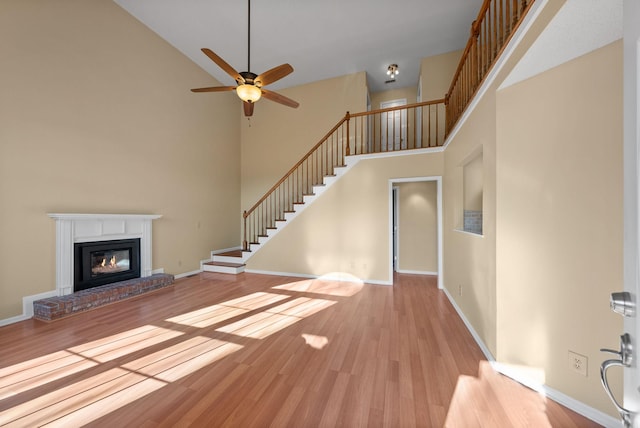 unfurnished living room with a brick fireplace, a towering ceiling, ceiling fan, and light hardwood / wood-style flooring