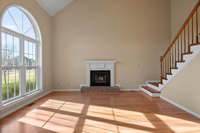 unfurnished living room featuring light hardwood / wood-style floors, high vaulted ceiling, and a brick fireplace