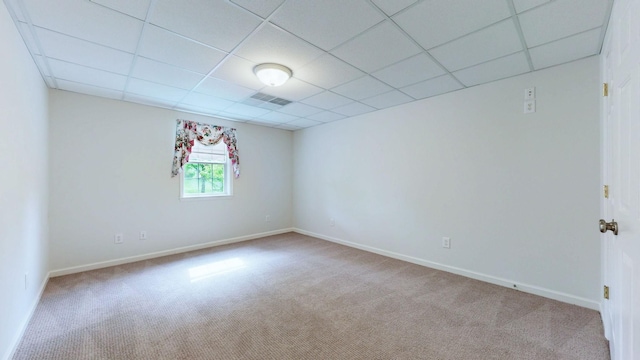 carpeted empty room with visible vents, a drop ceiling, and baseboards