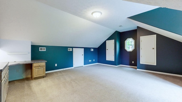 additional living space with baseboards, visible vents, light colored carpet, and vaulted ceiling
