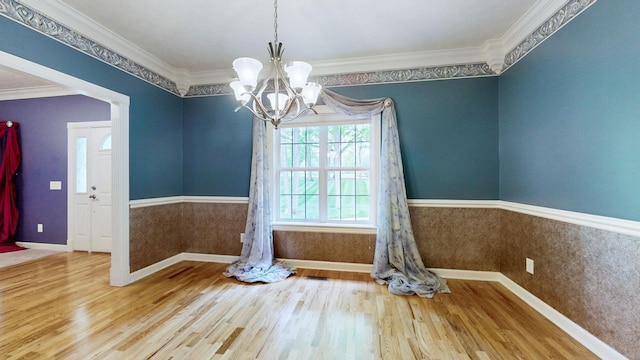 unfurnished dining area featuring an inviting chandelier, wood finished floors, crown molding, and baseboards