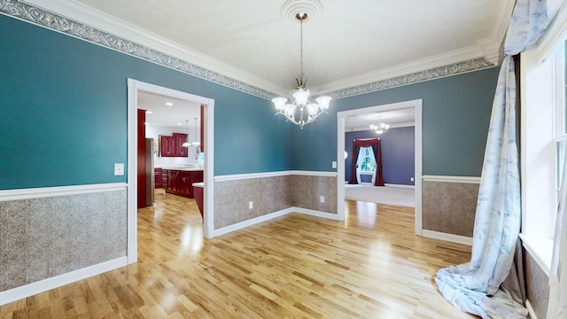 unfurnished dining area with a chandelier, a wainscoted wall, and crown molding