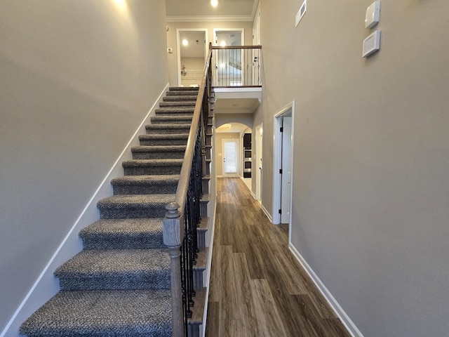 staircase featuring a towering ceiling, wood-type flooring, and ornamental molding