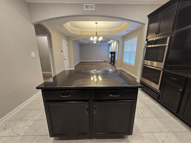 kitchen featuring a tray ceiling, double oven, a kitchen island, and dark stone countertops