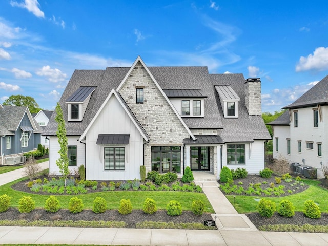 view of front facade with metal roof, a shingled roof, board and batten siding, a standing seam roof, and a chimney