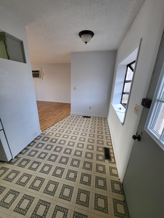 unfurnished dining area featuring light floors, a wall mounted air conditioner, and a textured ceiling