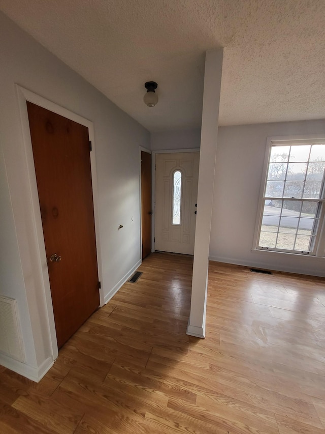 foyer with light wood-style floors, baseboards, a textured ceiling, and visible vents