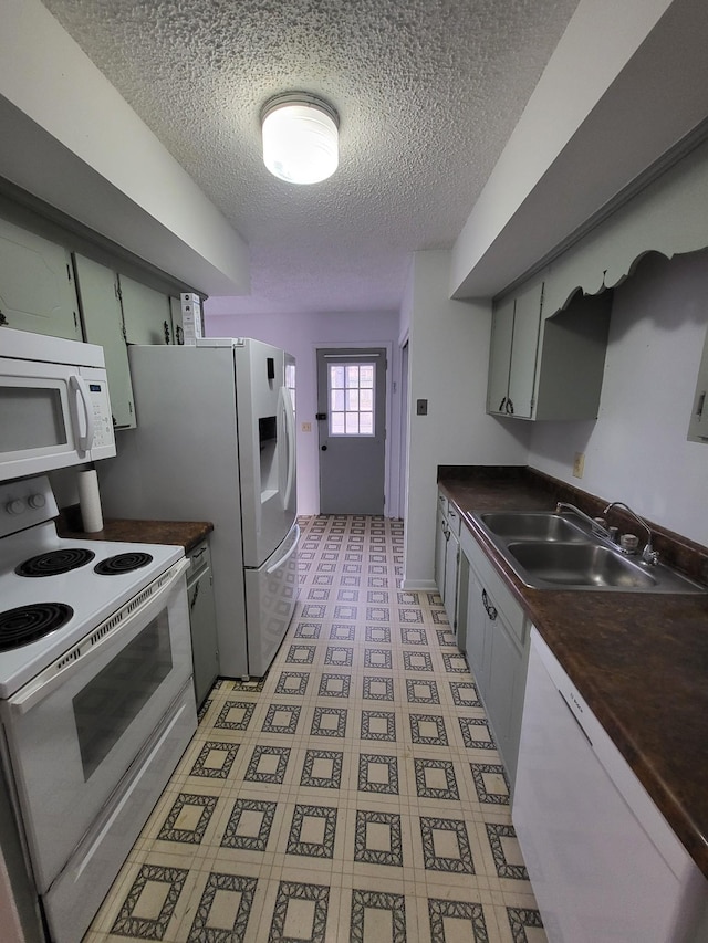 kitchen featuring a textured ceiling, dark countertops, a sink, light floors, and white appliances