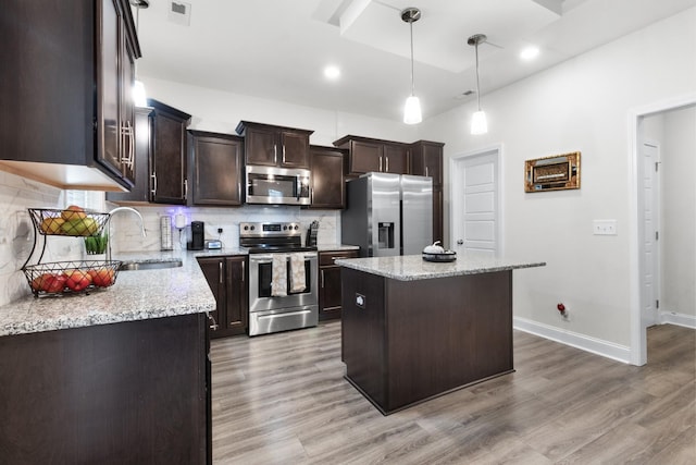 kitchen with sink, stainless steel appliances, a center island, and light stone countertops