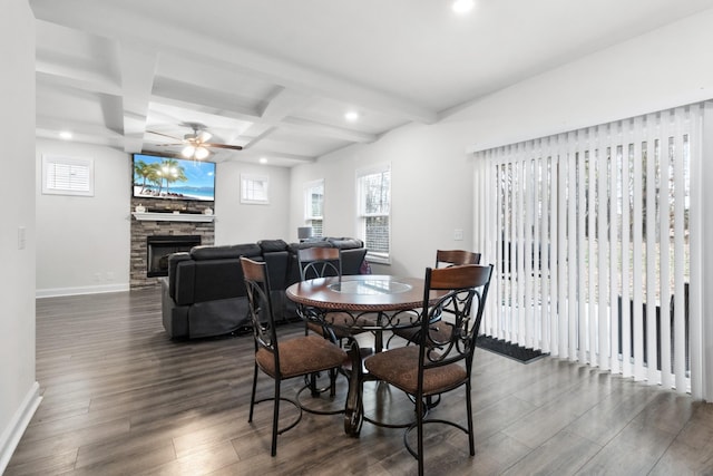 dining room featuring a stone fireplace, beamed ceiling, coffered ceiling, ceiling fan, and dark wood-type flooring