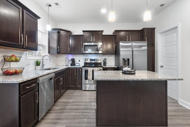 kitchen featuring sink, light hardwood / wood-style flooring, appliances with stainless steel finishes, a kitchen island, and pendant lighting