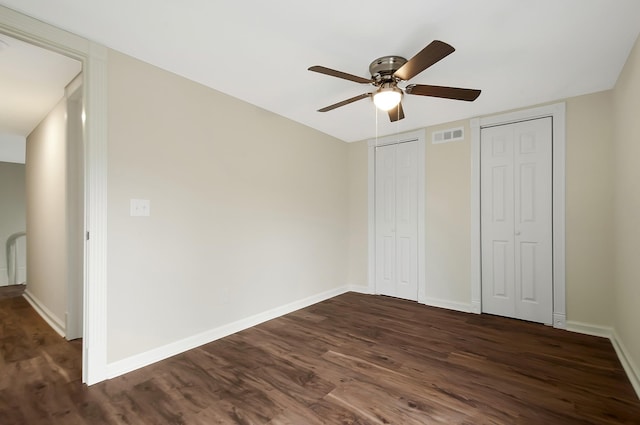 unfurnished bedroom with multiple closets, ceiling fan, and dark hardwood / wood-style flooring