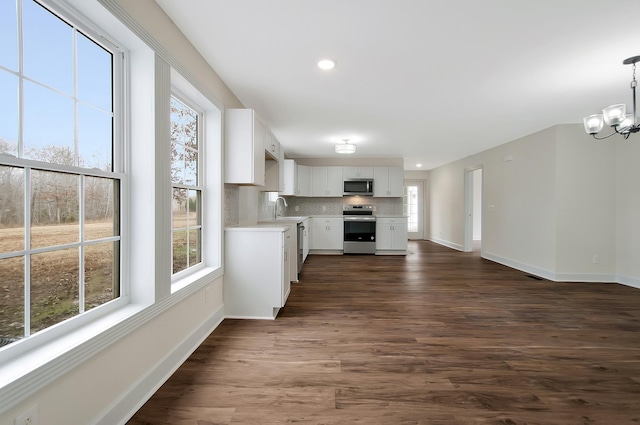 kitchen featuring dark wood-type flooring, white cabinetry, appliances with stainless steel finishes, pendant lighting, and decorative backsplash