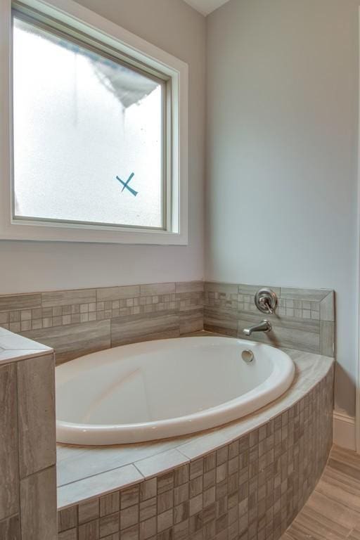 bathroom featuring tiled tub, plenty of natural light, and wood-type flooring