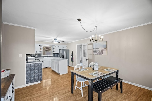 dining space with ornamental molding, sink, ceiling fan with notable chandelier, and light wood-type flooring