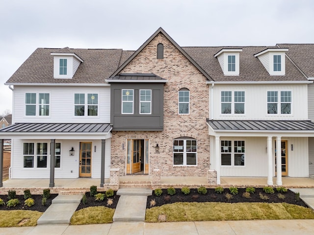 view of front facade featuring a porch, a standing seam roof, brick siding, and a shingled roof