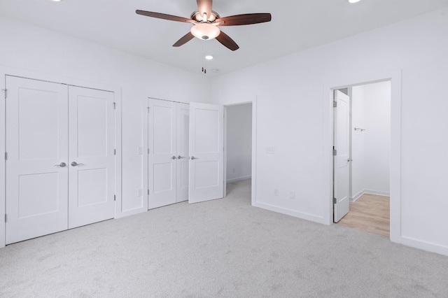 unfurnished bedroom with light carpet, two closets, connected bathroom, and ceiling fan