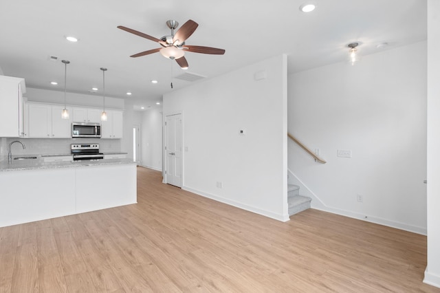 kitchen with light stone counters, decorative light fixtures, light hardwood / wood-style flooring, appliances with stainless steel finishes, and white cabinets