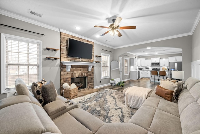 living room featuring hardwood / wood-style flooring, ceiling fan, ornamental molding, and a fireplace