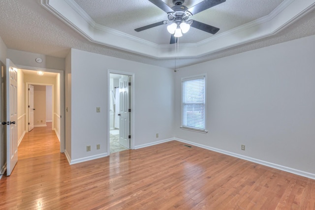 unfurnished bedroom with a tray ceiling, ceiling fan, light hardwood / wood-style floors, crown molding, and a textured ceiling