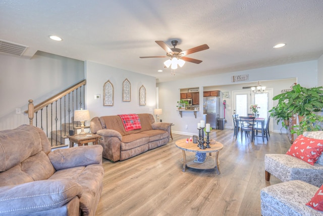 living room with ceiling fan with notable chandelier, light hardwood / wood-style floors, and a textured ceiling