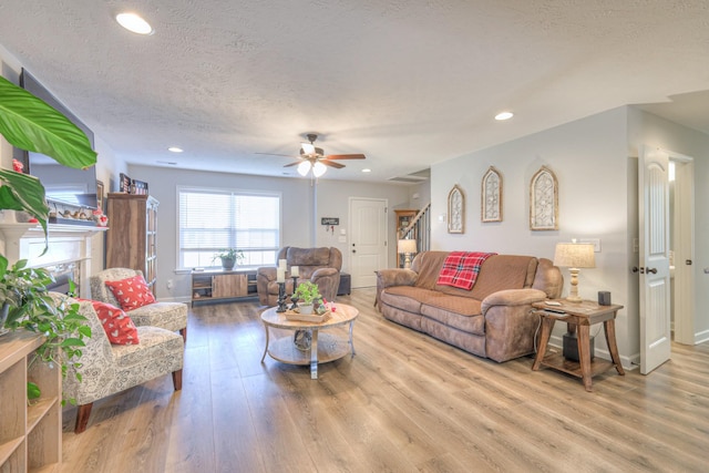 living room with a textured ceiling, ceiling fan, and light hardwood / wood-style floors