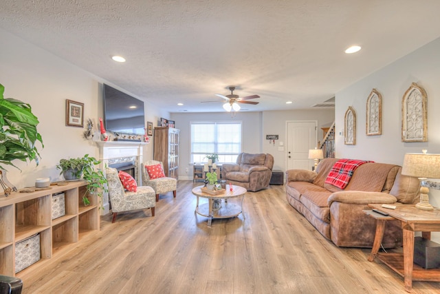 living room with ceiling fan, light wood-type flooring, and a textured ceiling