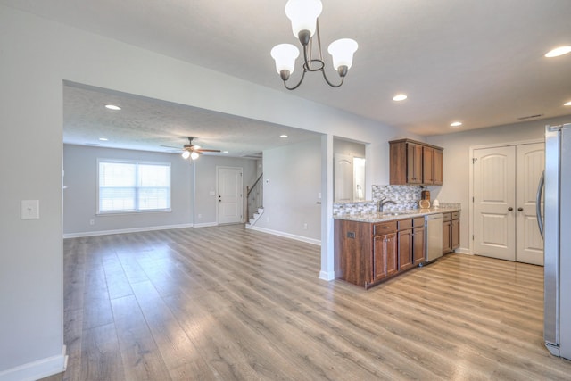 kitchen featuring open floor plan, stainless steel appliances, baseboards, backsplash, and light wood-style flooring