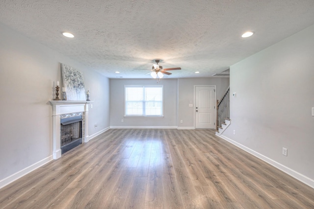 unfurnished living room featuring baseboards, stairs, a fireplace, wood finished floors, and a ceiling fan