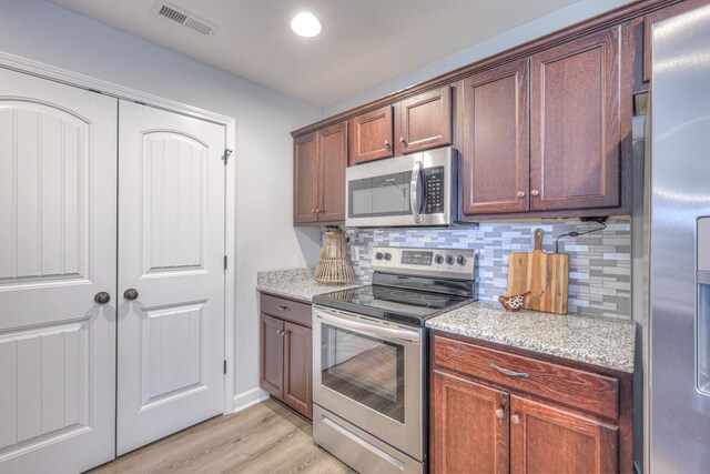 kitchen featuring light stone counters, light wood-style flooring, stainless steel appliances, visible vents, and decorative backsplash