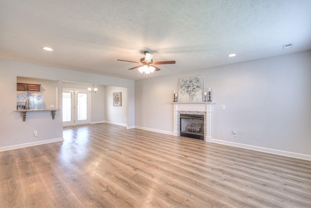 unfurnished living room featuring visible vents, baseboards, a fireplace, light wood-type flooring, and ceiling fan with notable chandelier