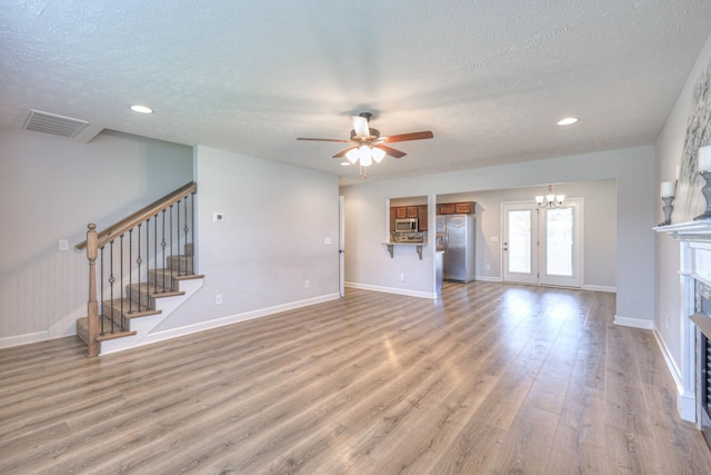 unfurnished living room with a textured ceiling, stairway, light wood-type flooring, and ceiling fan with notable chandelier