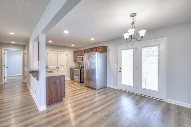kitchen with stainless steel appliances, light stone counters, light wood finished floors, a peninsula, and a notable chandelier