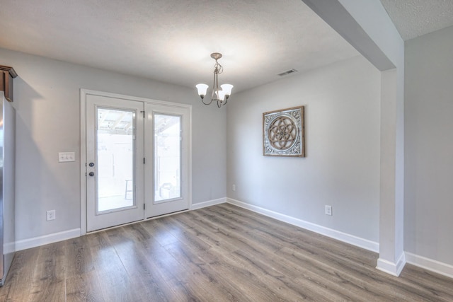 unfurnished dining area featuring a notable chandelier, wood finished floors, a textured ceiling, baseboards, and visible vents