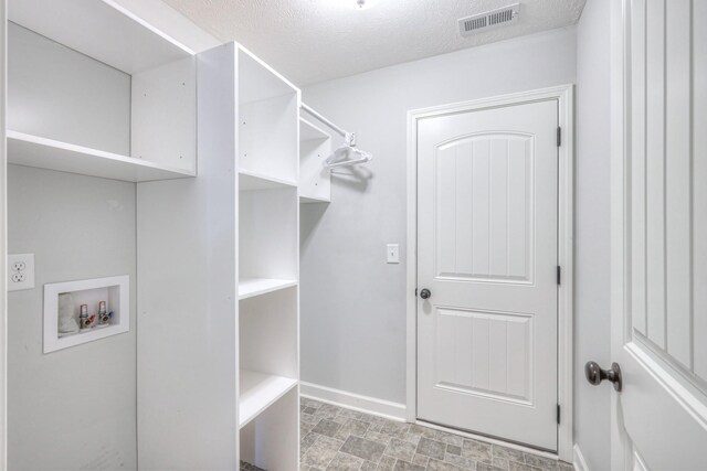 clothes washing area with a textured ceiling, visible vents, washer hookup, baseboards, and laundry area