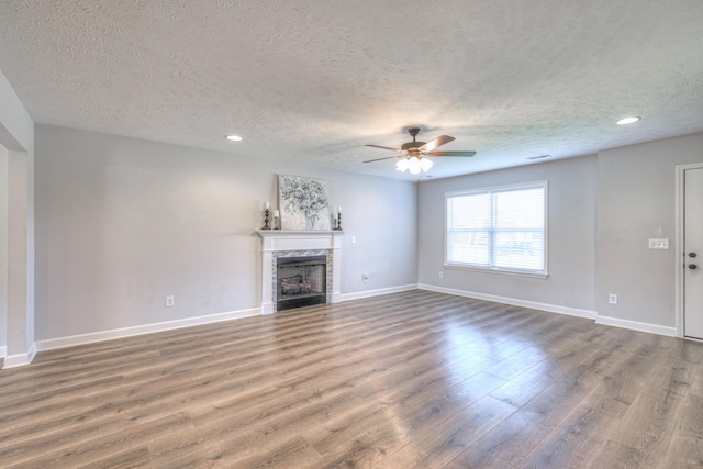 unfurnished living room featuring baseboards, a textured ceiling, a ceiling fan, a tile fireplace, and wood finished floors