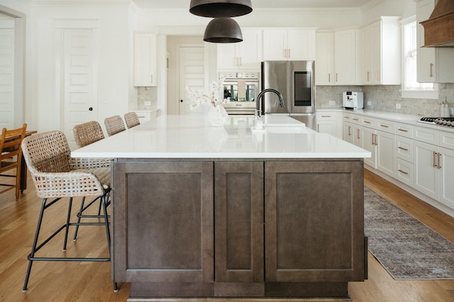 kitchen featuring white cabinetry, stainless steel appliances, a breakfast bar, and a large island with sink